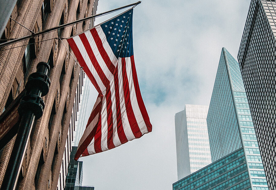 The USA or united states of america flag on a flagpole near skyscrapers under a cloudy sky